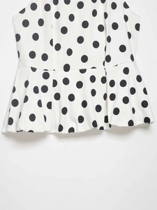 Détail du haut sans manches blanc à basque avec motif classique à pois noirs élégants