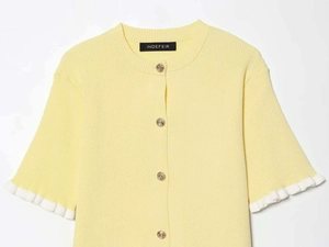 Detail of yellow knit cardigan with golden relief buttons and white ruffled cuffs