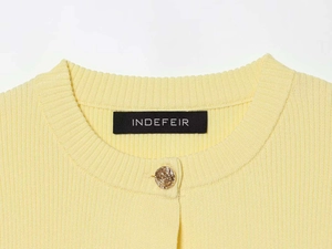 Detail of soft cream yellow ribbed knit texture and gold spiral button on women cardigan