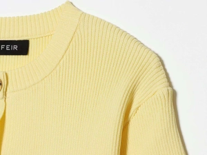 Detailed macro view of the cream yellow ribbed knit texture and gold button fastener