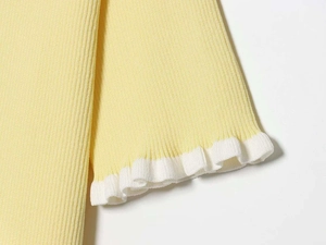 Detail of cream yellow ribbed knit fabric with white ruffled edge trimming