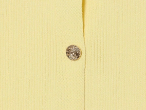 Macro view of light yellow ribbed knit fabric featuring detailed gold metallic buttons
