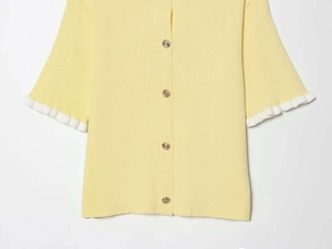 Detail of yellow ribbed knit cardigan featuring white ruffle cuffs and gold buttons