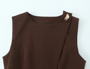 Detail view of dark brown sleeveless top featuring a wavy gold decorative button and round neck
