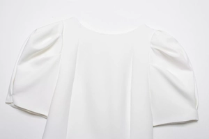 Close-up of a white puff sleeve top with a round neckline and pleated shoulder details