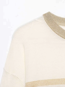Close-up of cream knit sweater showing gold metallic trim on the neckline and fabric texture