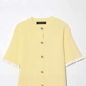 Pale yellow knit cardigan with gold buttons and white ruffled sleeves on plain background