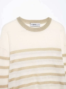 Close-up of white knitted sweater featuring elegant golden metallic horizontal stripes