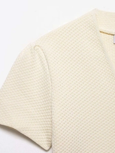 Gros plan sur la texture du gilet en maille crème avec col en V et motif gaufré élégant
