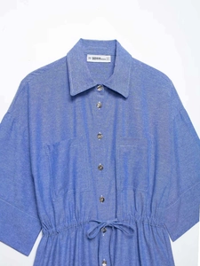 Dettaglio in piano di un abito a camicia blu con coulisse in vita e bottoni metallici