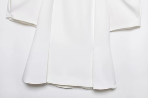 Detailed view of puff sleeves and pleated hem on white minimalist cotton top