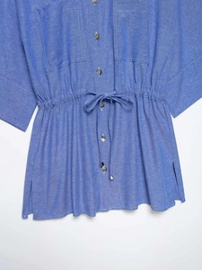 Dettaglio della camicia blu con coulisse in vita, bottoni metallici e spacco laterale
