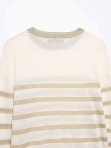 Detailed view of white knit sweater with elegant horizontal gold metallic stripes