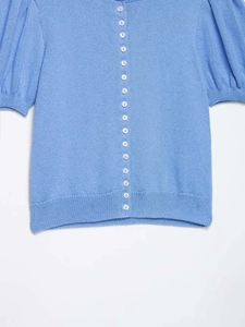 Détail d'un cardigan en maille bleu clair avec manches bouffantes et boutons perles