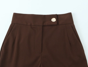 Detail of high-waist dark brown trousers featuring a textured gold button and side pockets