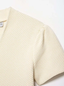Détail du tissu en maille crème avec col en V et étiquette de taille S
