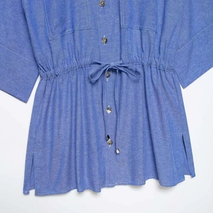 Camicia blu con coulisse in vita, cuciture bianche a contrasto e bottoni in metallo