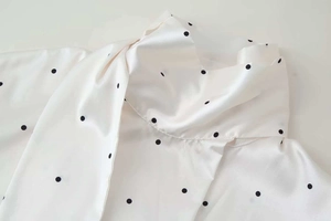 Close-up of the standing collar and smooth satin fabric on the white polka dot shirt
