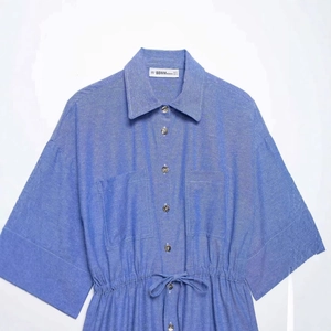 Abito a camicia stile denim blu con coulisse in vita e tasche sul petto su fondo grigio