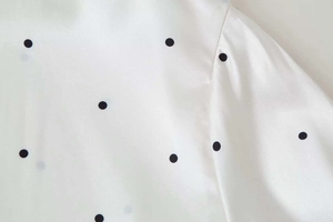 Detailed close-up of cream satin fabric with classic black polka dot pattern prints