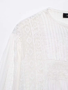 Details einer weißen Baumwollbluse mit feiner Spitze und plissierten Stoffstrukturen