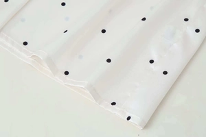 Detailed close-up of white polka dot chiffon fabric with black spots and fine stitching