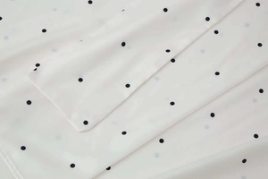 Close-up of white chiffon fabric with black polka dots showing soft texture and fine stitching