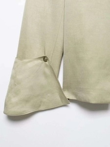 Detail of light green shirt cuff featuring an asymmetrical fold and embossed gold button