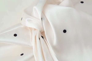 Close-up detail of smooth satin fabric with elegant black polka dot pattern and silky texture