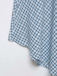 Détail du tissu à carreaux bleu clair avec ourlet asymétrique et texture tissée fine