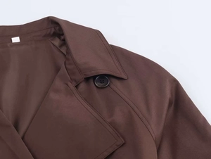 Detail of coffee brown trench coat showing lapel, button, and textured twill fabric