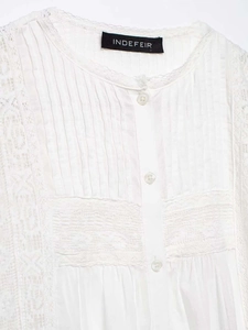 Detail der weißen Spitzenbluse mit vertikalen Falten und floralen Stickereien am Saum