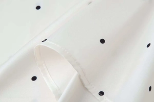 Detailed macro view of white chiffon fabric with black polka dots and high-quality stitching