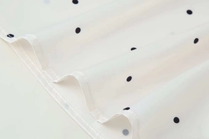 Detailed macro view of white chiffon fabric featuring classic black polka dots with neat hems