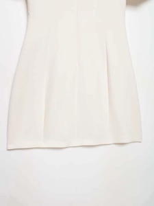 Détail de la robe courte minimaliste blanc cassé avec texture tissée et plis verticaux