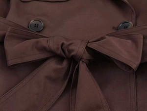 Detailed view of the double-breasted buttons and bow belt on a dark brown trench coat