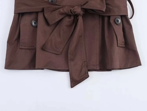 Close-up of a brown trench coat waist featuring a tied belt and decorative black buttons