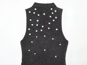 Dettaglio del top in maglia senza maniche grigio scuro con bottoni decorativi bianchi