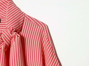 Detail of pink and beige striped poplin shirt featuring a large neck tie bow design