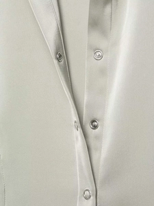Macro shot of silver satin shirt showing detailed metal snap button closure and fabric