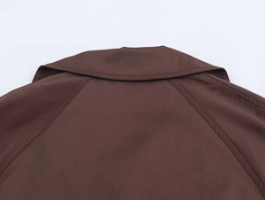 Detail view of the lapel collar and raglan sleeve seams on a brown trench coat
