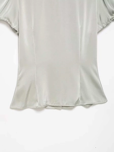 Detail of sage green satin blouse showing the gathered waistline and smooth fabric texture