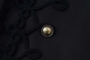 Detail of hussar-style braiding and vintage bronze metal button on black blazer jacket
