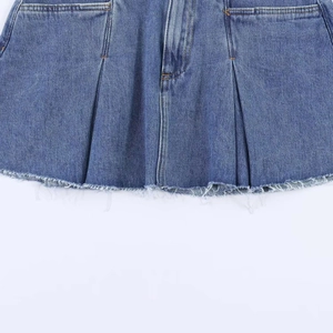 Detail of blue denim skirt featuring double pleats and natural frayed fringe hemline