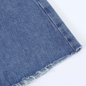 Close-up of raw fringe hem and twill texture on high-waist vintage blue denim skirt