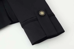 Detail of black blazer cuff with decorative strap, bronze metal button and topstitching
