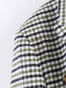 Detail view of green plaid tweed blazer shoulder with fabric texture and brown button