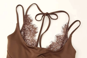 Detail eines dunkelbraunen Strick-Bodys mit feiner Wimpernspitze und Schleifendetails