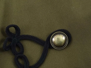 Detail of army green twill fabric with vintage bronze metal button and black rope knot