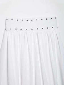 Detail of white midi skirt featuring double-row silver rivets and pleated waistline
